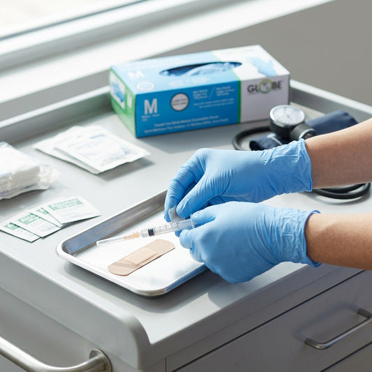 Globe 4 mil sky blue nitrile medical gloves worn by a professional preparing a medical tray.
