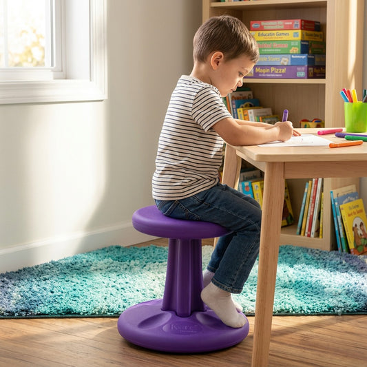 Toddler sitting on a purple Kore Wobble Stool while drawing at a wooden desk in a bright playroom.