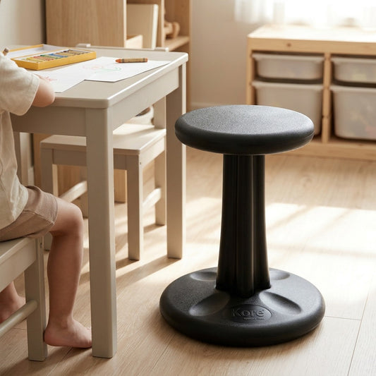 Black 40cm fdmt Kore Wobble Stool for active sitting, shown in a bright playroom by a child's desk.