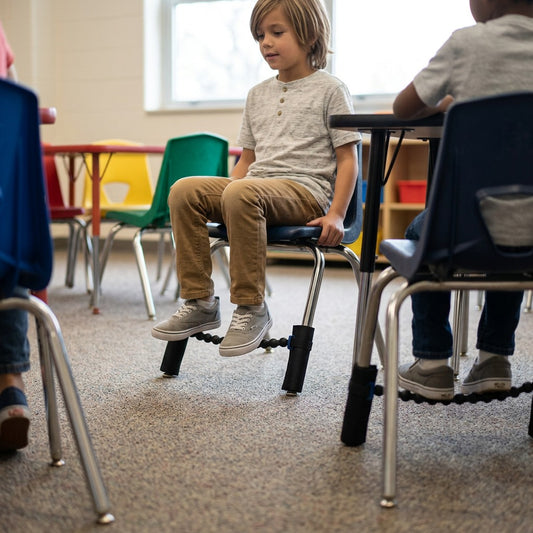 A student uses the fdmt Universal Bouncy Band on a classroom chair to fidget while sitting at a desk.